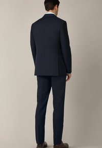 Granatowy garnitur z pojedynczym rozcięciem, wyraźnymi ramionami i dopasowanym krojem. Spodnie mają gładki przód i prasowane kanty. Gładka faktura materiału.