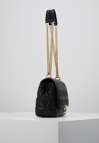 Kvalitní černá kožená taška s prošíváním a zlatými řetízkovými popruhy, má obdélníkový tvar a strukturovaný diamantový vzor. Hladký povrch a zlaté kování.