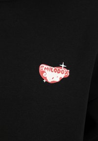 T-shirt noir avec un petit logo graphique rouge et blanc sur la poitrine gauche, doté d'une texture de tissu lisse et d'un design minimaliste.