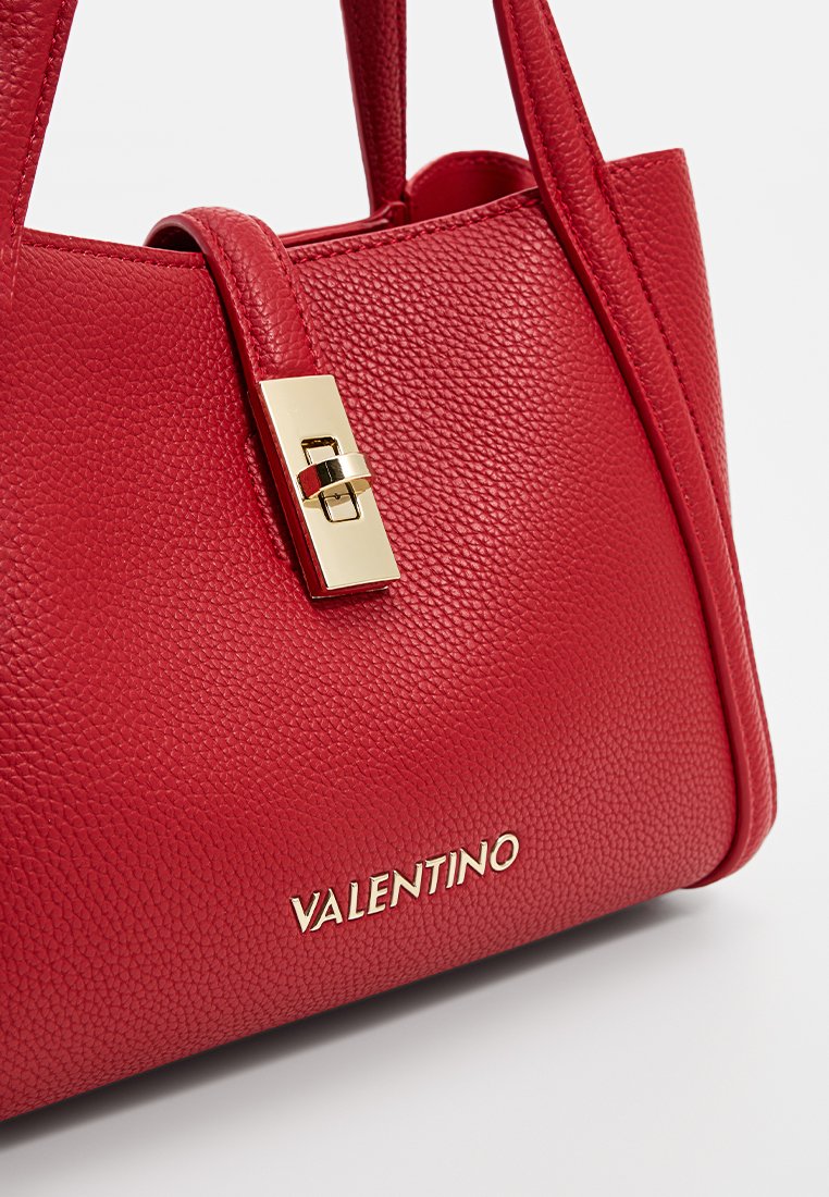 Sac à main en cuir rouge avec une surface texturée, un fermoir en métal doré et un nom de marque prominent embossé sur le devant.