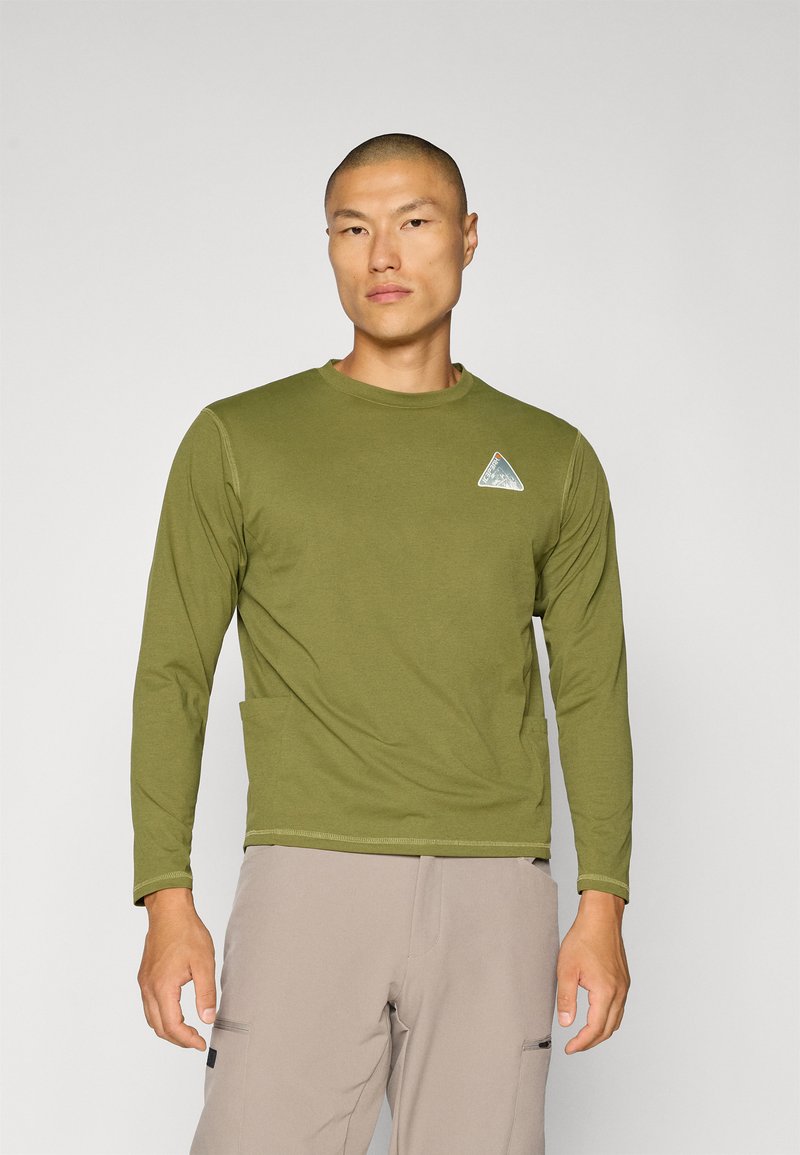 Olivegrünes Langarmshirt mit Rundhalsausschnitt, mit einem dreieckigen Logopatch auf der linken Brust und einer Brusttasche. Glatte Textur.