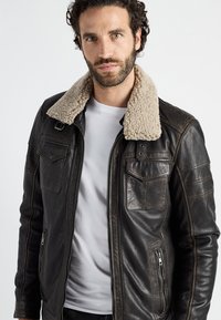 Bruine leren jas met een beige schapenvacht kraag, ritssluitingen in de zakken en een gladde textuur. Beschikt over een rechte pasvorm en contrasterende stiksels.