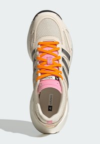 Beiger Sportschuh mit Netz-Obermaterial, schwarzen Akzenten und orangefarbenen Schnürsenkeln. Verfügt über eine rosa Zunge und eine strukturierte Sohle. Adizero-Branding sichtbar.