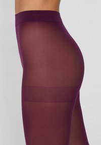 Leggings bordeaux con una vita alta e una texture semi-trasparente. Presentano una superficie liscia con una leggera lucentezza e un colore uniforme.