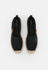 Svart canvas slip-on skor med en texturerad jutesula och tan läderdetalj, med rund tå och elastisk sida för enkel användning.