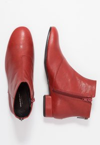 Rote Leder-Stiefeletten mit glatter Oberfläche, runder Zehenform und seitlichem Reißverschluss. Niedriger Blockabsatz und minimalistisches Design.