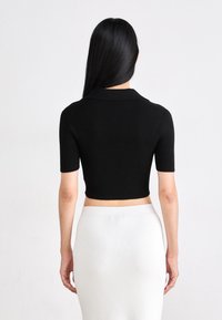 Top scurt negru cu model canelat, cu guler, mâneci scurte și un design ajustat. Asortat cu o fustă canelată gri deschis cu talie înaltă.