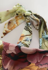 Floral-patterned fabric tied in a loose knot with colors including yellow, brown, green, blue, and dark red on a light background.