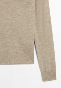 Helle beige Pullover mit langen Ärmeln, der Textur und Nahtdetails auf einem weißen Hintergrund zeigt.