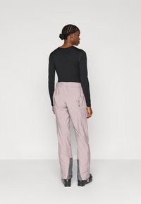 Világos lila oldalzsebes terepnadrágok szürke részletekkel, fekete, testhezálló hosszú ujjú felsővel párosítva; sima anyagtextúra.