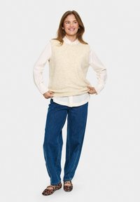 Beige ull utan ärmar tröja över en vit skjorta med krage, i kombination med lösa blå denim jeans och bruna leopardmönstrade ballerinaskor.