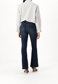 Flared denimjeans i mörkblå tvätt med en mjuk struktur. Har två bakfickor och en märkesetikett vid midjan. I kombination med en randig skjorta.