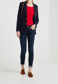 Marinblazer med guldknappar, röd kortärmad topp, mörkblå skinny jeans och bruna mockaloafers. Uppvikt nederkant på jeansen.