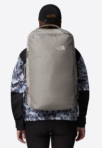 Gray backpack with a smooth texture, featuring a logo in the upper left, carried on a person wearing a patterned jacket.