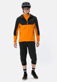 Completo da ciclismo maschile che include una giacca leggera zip-up nera e arancione, pantaloni corti neri, ginocchiere e un casco nero.