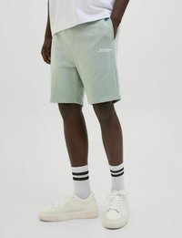 Lichtgroene katoenen shorts met zijzakken, voorzien van een wit geborduurd logo. Gecombineerd met witte sneakers en zwartgestreepte crew-sokken.