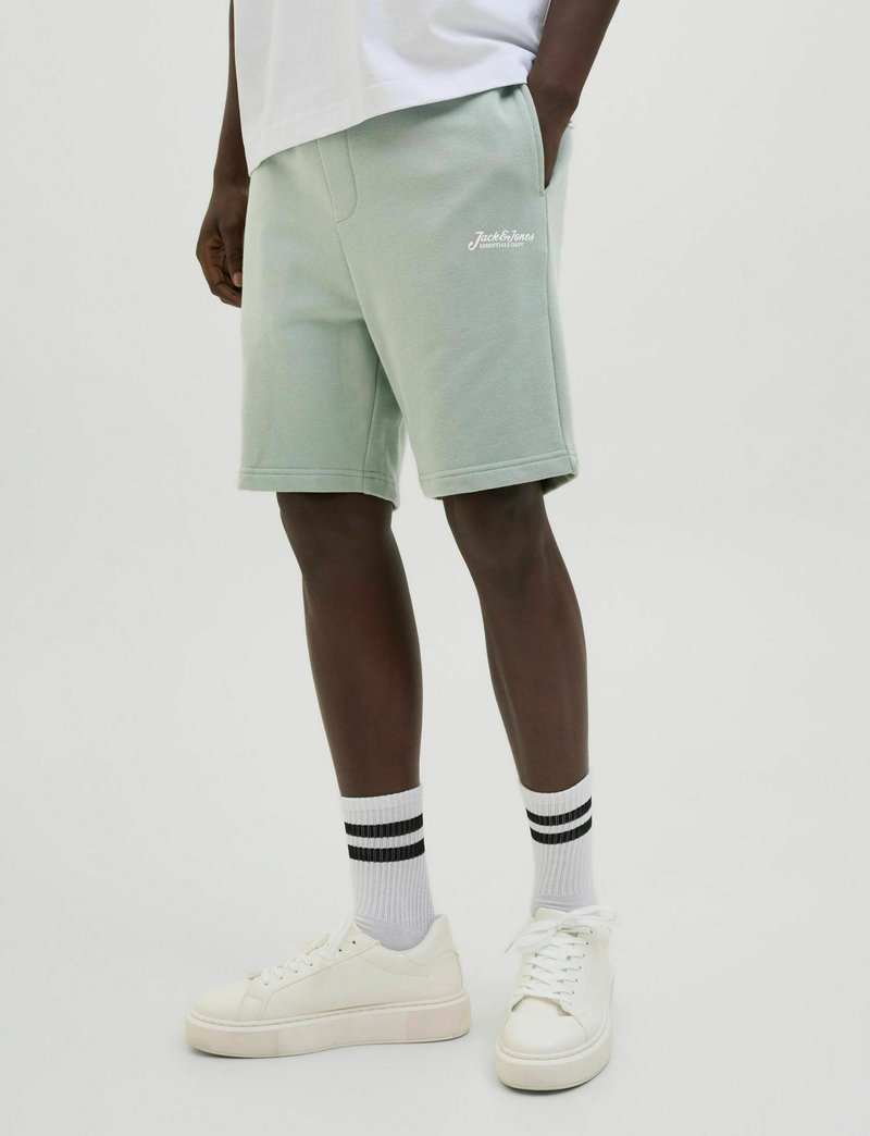 Lichtgroene katoenen shorts met zijzakken, voorzien van een wit geborduurd logo. Gecombineerd met witte sneakers en zwartgestreepte crew-sokken.
