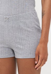 Grå bomullsshorts med en teksturert mønster, med vertikale striper og små utskjæringsdetaljer. Inkluderer en dekorativ sløyfe i midjen.