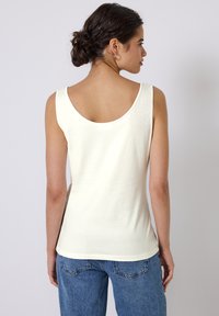 Haut sans manches jaune clair avec un col rond, texture douce et silhouette ajustée, associé à un jean en denim.