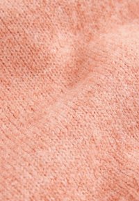 Miękka, teksturowana tkanina w jasnym odcieniu brzoskwini z dzianinowym wzorem i delikatnym puszeniem, co tworzy przytulny i ciepły wygląd.