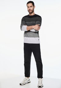 Šedý pruhovaný svetr s černými a světle šedými tóny, v kombinaci s černými kalhotami a bílými teniskami. Jednoduchý kulatý výstřih a manžety.