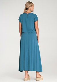 Turkusowy, luźny, dwu-elementowy zestaw składający się z bluzki z krótkim rękawem i maxi spódnicy. Wykonany z lekkiego materiału z zapięciem z tyłu.