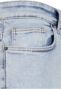 Svijetloplave traperice imaju stražnji džep s vidljivim šavovima i brončanim detaljima. Tekstura pokazuje mekan, istrošen izgled.