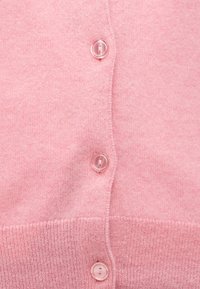 Tissu tricoté rose avec trois boutons translucides alignés verticalement sur un bord côtelé d'un vêtement.