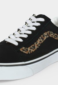 Baskets noires avec lacets blancs, semelle blanche et une bande imprimée léopard sur le côté.