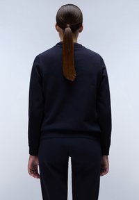 Marineblauwe sweater met een ronde halslijn en geribbelde manchetten, gecombineerd met bijpassende broek. Glad materiaal, aansluitend ontwerp, minimale details.