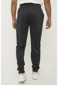 Zwarte sportbroek met een elastische tailleband, taps toelopende benen en zijzakken, gecombineerd met witte sneakers. Soepele, lichte stof.