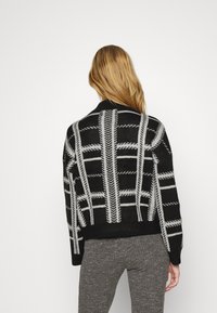 Sweter w czarno-szary wzór z wysokim kołnierzem, z siatką w kratę oraz ściągaczami na mankietach i dolnej krawędzi. Miękka tekstura i luźny krój.