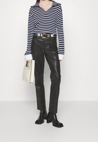 Marineblauw en witte gestreepte lange mouw top met v-hals, zwarte leren aansluitende broek, zwarte hoge laarzen en crèmekleurige handtas.