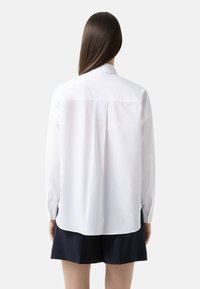 Witte lange mouwen shirt met een button-down kraag, details met een rugplooitje en een ronde zoom. De stof lijkt glad met een klassieke pasvorm.