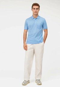 Polo azzurro chiaro con colletto e maniche corte, abbinata a pantaloni crema, larghi, e sneakers con dettagli decorati.