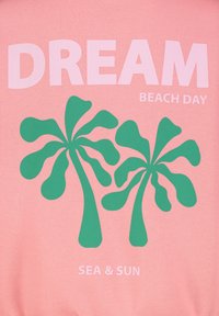 Rosa Sweatshirt mit auffälligem weißen Text "DREAM BEACH DAY" und grünen Palmenmotiven. Weicher Stoff mit glatter Textur.