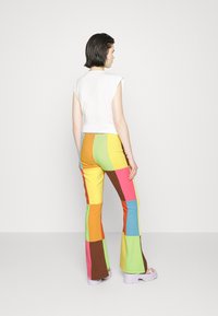 Top branco sem mangas combinado com calças flare de retalhos multicoloridos apresentando seções em laranja, rosa, verde, amarelo e castanho. Sapatos chunky em tons pastel.
