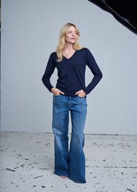 Pull col en V bleu marine associé à un jean évasé bleu, avec une texture douce et une coupe décontractée. L'arrière-plan est uni et de couleur claire.