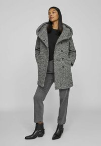 Gray and black patterned coat with a large hood and double-breasted buttons, worn over a black top, paired with gray pants and black ankle boots.