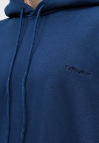 Granatowa bluza z kapturem wykonana z miękkiego materiału, z kapturem ze sznureczkiem i dyskretnym haftowanym logo na piersi.