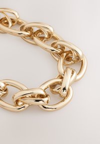 Gold-colored chain necklace featuring interlocking oval links with a smooth, shiny surface and rounded edges.