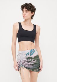 Top cropped negro y falda mini gris con un diseño gráfico. La falda presenta un lado fruncido con cordón y acentos de texto.