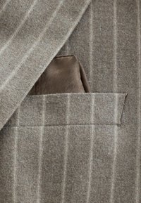 Brown striped suit fabric with a light texture, featuring a brown pocket square patterned with subtle tonal designs, tucked into the breast pocket.