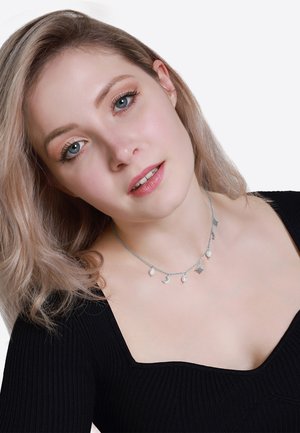 Collier en argent avec des charms lune et étoile, orné de petites perles, porté avec un haut noir à côtes. Le design est délicat et complexe.