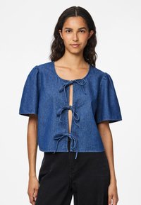 Τζιν μπλούζα σε σκούρο μπλε με κοντά φουσκωτά μανίκια, με ανοιχτό εμπρός κλείσιμο που διαθέτει τρεις φιόγκους, και με κοντή γραμμή. 