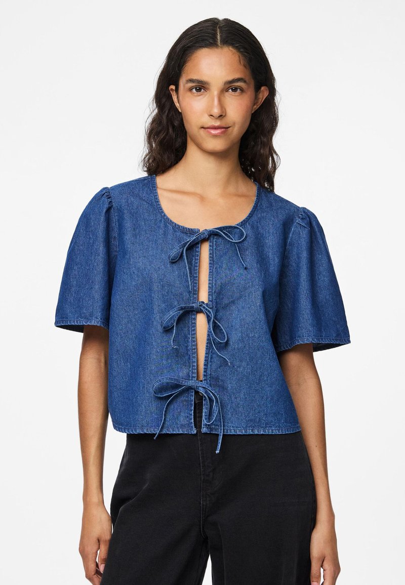 Τζιν μπλούζα σε σκούρο μπλε με κοντά φουσκωτά μανίκια, με ανοιχτό εμπρός κλείσιμο που διαθέτει τρεις φιόγκους, και με κοντή γραμμή.