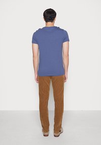 Modré bavlněné tričko s krátkým rukávem v kombinaci s hnědými manšestrovými kalhotami. Viditelná struktura na kalhotách; jednoduché, jednobarevné.