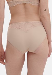 Biancheria intima beige con un bordo in pizzo lungo la parte superiore. Materiale liscio con una vita leggermente strutturata, caratterizzata da un motivo decorativo.