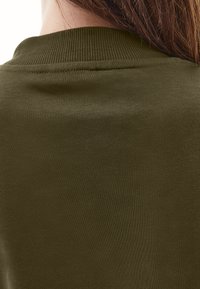 Ciemnooliwkowa bawełniana tkanina z prążkowanym dekoltem, gładką fakturą i minimalną liczbą szwów. Skoncentrowano się na widoku z tyłu i detalach materiału.