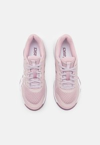 Zapatillas deportivas de color rosa claro con parte superior de malla, puntera reforzada, diseño con cordones y suela blanca. Presenta un logo en la lengua y patrones texturizados.